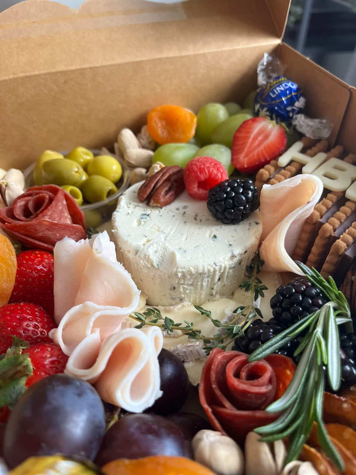 Close-up of a herbed cheese wheel, prosciutto, blackberries and pretzels