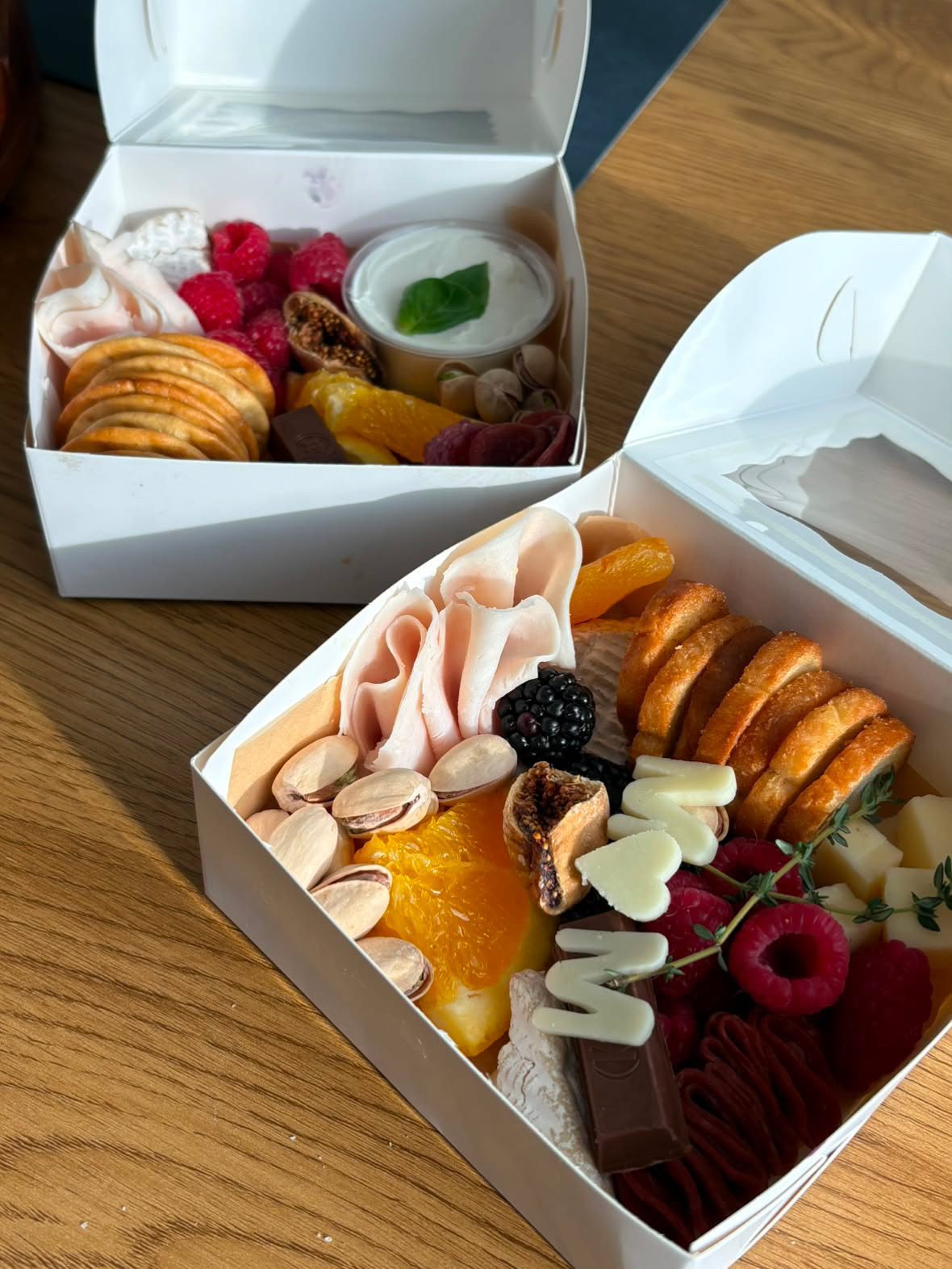 Two mini grazing boxes in sunlight with cured meats, brioche, cheese and fresh fruit — Around the Board Ottawa